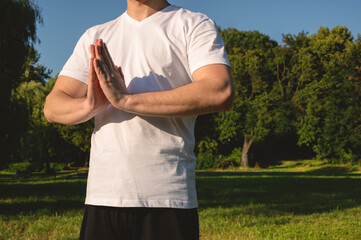  Man doing namaste yoga in the park on the sunny morning.  Man in white t shirt. Healthy and active...