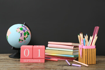 Different stationery, globe and calendar with date SEPTEMBER 1 on wooden table against black chalkboard