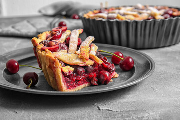 Plate with pieces of tasty cherry pie on grey background