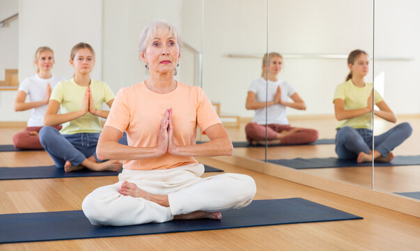 Group of people of different ages sitting in lotus position practicing meditation in yoga class - Powered by Adobe
