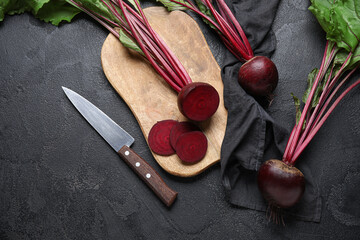 Cutting board with fresh cut beetroots and knife on black table