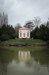 White monument with a beautiful architecture located on an islet with green spring grass, surrounded by a lake with clean water that has an old wooden boat on the shore.