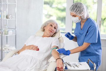 Obraz premium Elderly female patient preparing for intravenously injection at treatment room of clinic