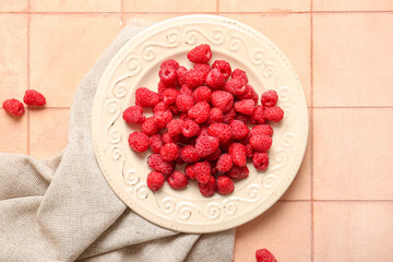 Plate with fresh raspberries on pink tile background