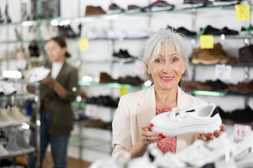Happy elderly woman choosing training shoes in shoe store.