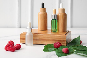 Fototapeta na wymiar Wooden podium with bottles of cosmetic raspberry oil on white background