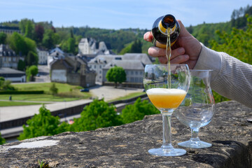 Pouring of blond strong Belgian abbey beer in to glass in sunny day with nice view on old town...