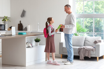 Father helping his little daughter to pack schoolbag in kitchen