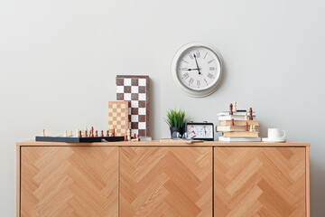 Chess boards with books and clock on chest of drawers in room