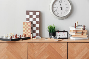 Chess boards with books and clock on chest of drawers in room