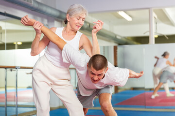 Elderly woman is training with man on the self-defense course in gym