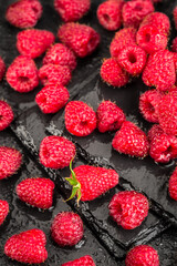 Wet red raspberries on a black slate background