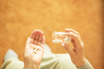 Close up of old female hands holding pills and puoring capsules from the bottle.