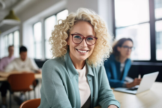 Generative AI image of portrait of smiling young female blondie employee in eyeglasses looking at camera while sitting at table in blurred office with working colleague on laptop