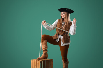 Beautiful female pirate with rope and wooden box on green background