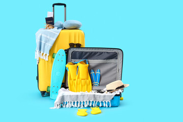 Suitcases with skateboard and different beach accessories on blue background. Travel concept