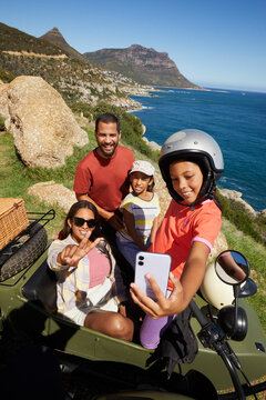 Young family with mom, dad and little girls taking a selfie with mountain backdrop during family vacation in Cape Town