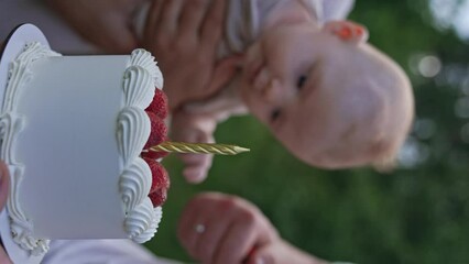 Beautiful creamy cake is given to a newborn baby. Male hand lighting a candle on the cake. Celebrating first month of child's life. Close up. Vertical screen.