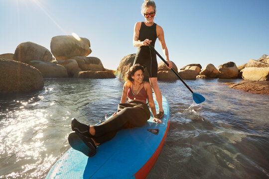 Young queer couple smiling and paddle boarding during sunset on the beach