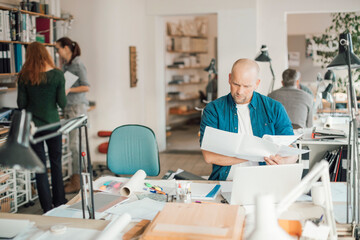 Mid adult man working in an startup company office with his coworkers behind him