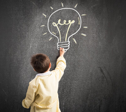Child draws with chalk on the blackboard a light bulb