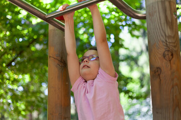 Fototapeta premium Little girl doing gymnastic exercises on the monkey bars in the park