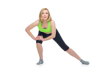 Fototapeta na wymiar Beautiful middle aged blond fit woman in green bra top and black pants doing sport exercise. Isolated over white background. Copy space.