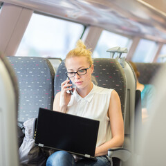 Businesswoman talking on cellphone and working on laptop while traveling by train. Business travel...
