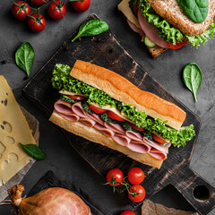 Delicious baguette sandwich with ham, bacon, cheese, lettuce, tomatoes, sausage, gammon on cutting...