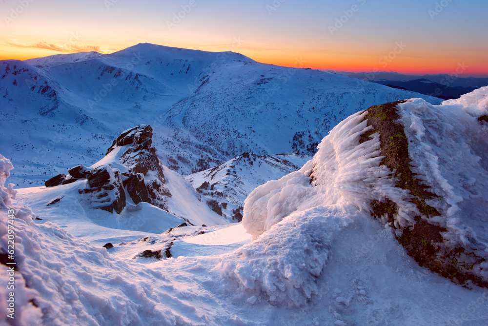 Sticker rock covered with snow in the midst of mountains and hot red sunlight