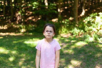 Fototapeta premium Little girl in glasses and pink t-shirt standing in the park