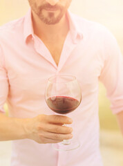Closeup toned image of glass with red wine.Sommelier in pink shirt holding glass with delicious red wine.