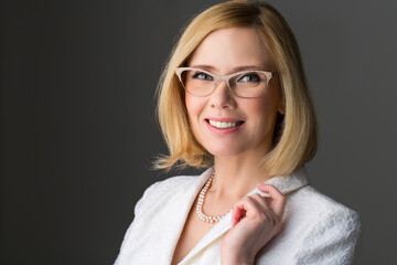 Closeup of elderly business woman in glasses. Happy smiling expression. Over grey background.