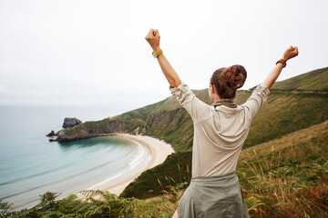 Into the wild in Spain. Seen from behind healthy woman hiker rejoicing in front of ocean view...