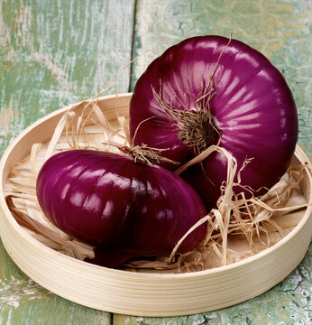 Two Raw Red Sweet Onion Full Body in Wicker Bowl closeup Cracked Wooden background