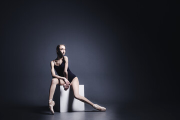 Fototapeta na wymiar Young ballerina in a black suit is dancing in a dark studio
