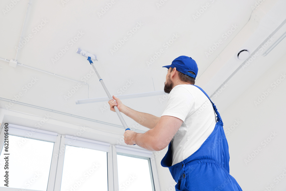 Canvas Prints Worker in uniform painting ceiling with roller on stepladder indoors, low angle view