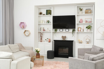 Stylish room interior with beautiful fireplace, TV set, armchairs, sofa and shelves with decor