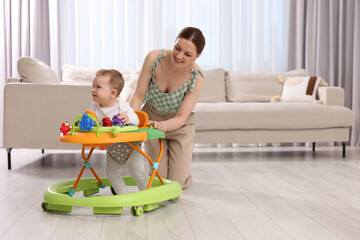 Cute boy making first steps with baby walker. Happy mother and her little son spending time together at home, space for text
