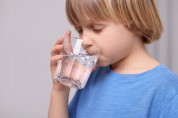 Cute little boy drinking fresh water from glass on grey background, closeup