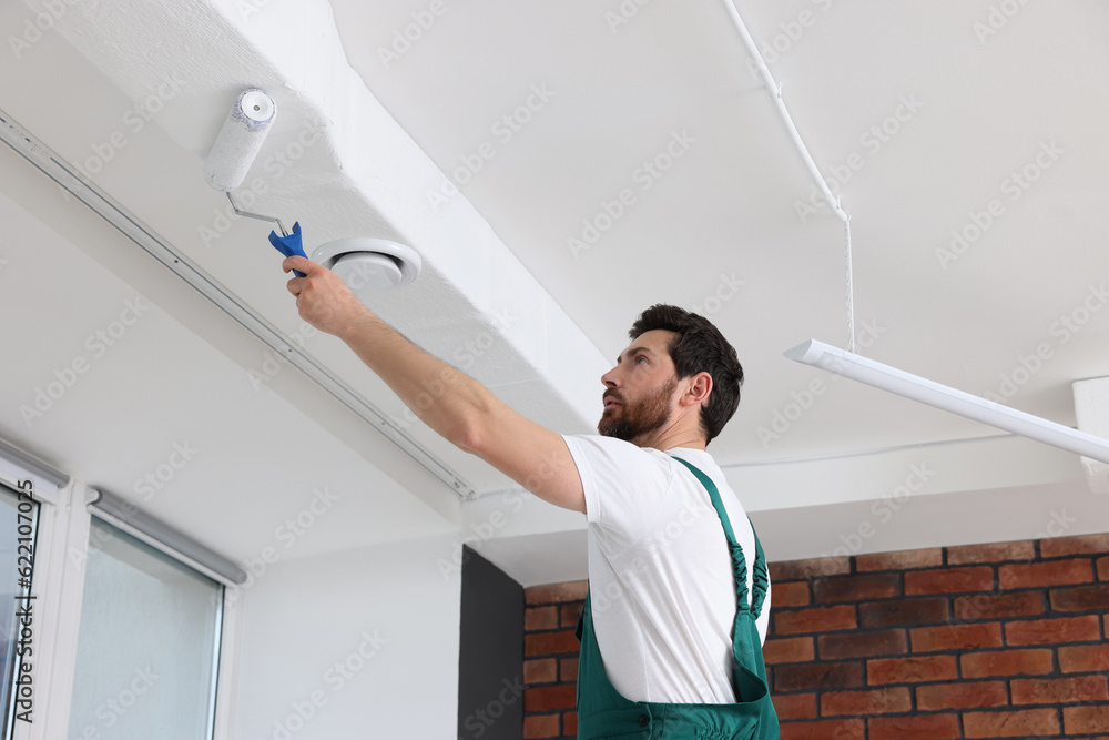 Poster Handyman painting ceiling with roller in room