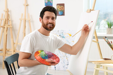 Happy man painting in studio. Using easel to hold canvas