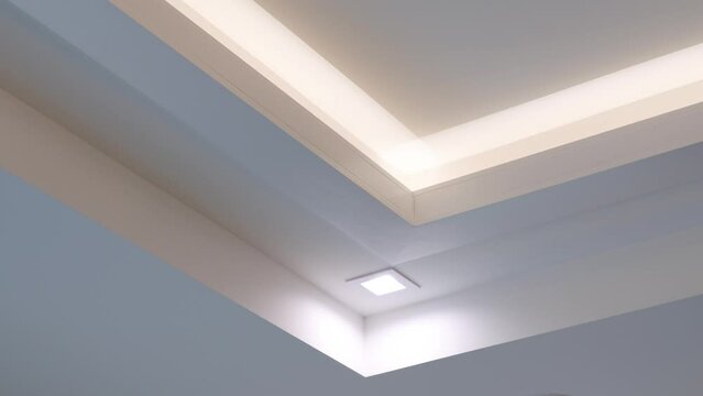 Drywall multi-level white ceiling with built-in led light and halogen lamp in new apartment. Modern design with fluorescent lighting
