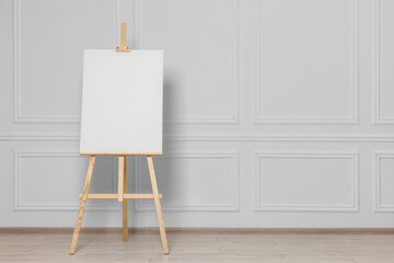 Wooden easel with blank canvas near white wall indoors. Space for text