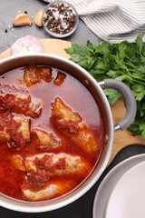 Delicious stuffed cabbage rolls cooked with homemade tomato sauce in pot and ingredients on grey table, flat lay