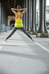 Fototapeta na wymiar Outdoors fitness in Paris. Seen from behind young woman jogger stretching on Pont de Bir-Hakeim bridge in Paris