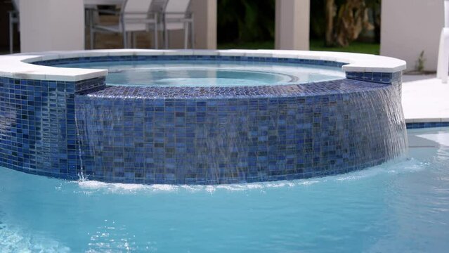 Residential inground swimming pool in backyard with crystal clear water running from artificial waterfall in house exterior. Concept of relaxation