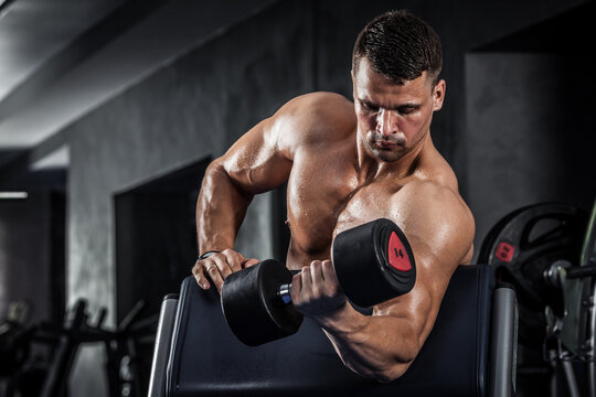 Brutal athletic man pumping up muscles with dumbbells