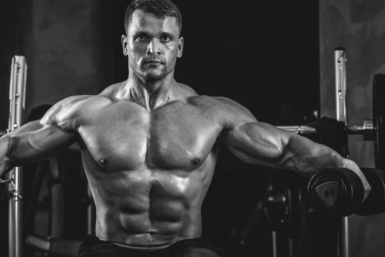 Brutal athletic man pumping up muscles with dumbbells in monochrome