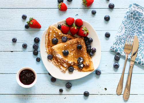 Delicious Crepes Breakfast with Dramatic light over a vintage wood background. An healthy meal of Pancakes with marmalede, blueberries and strawberries.